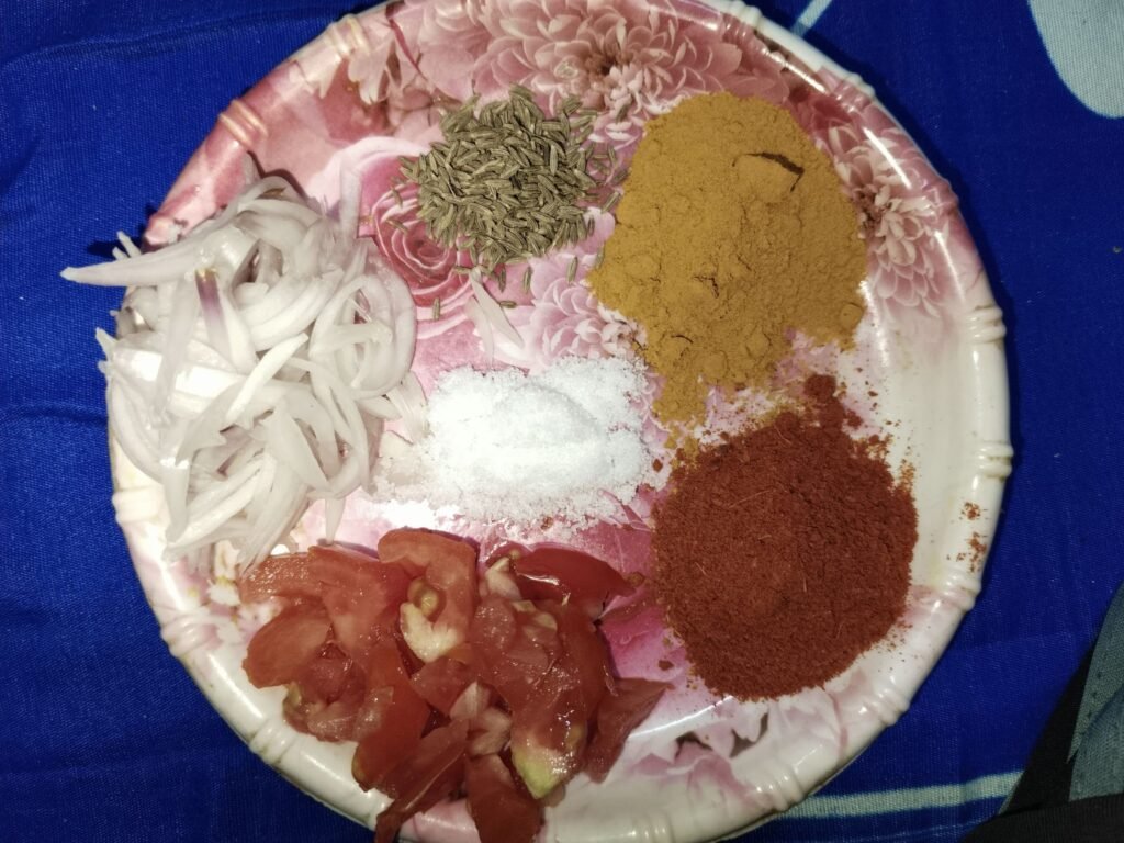 sliced onion chopped tomato red chilli powder turmeric cumin seeds and salt on a plate as spice mix for yellow rice