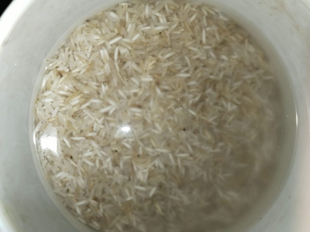 basmati rice soaking in water in a white bowl before cooking yellow rice recipe