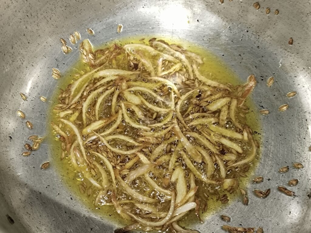 sliced onion and cumin seeds frying in hot oil in pan for yellow rice spice base