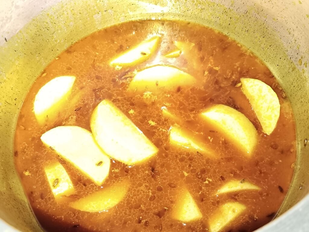 potato pieces cooking in yellow spiced masala base in a pot for yellow rice