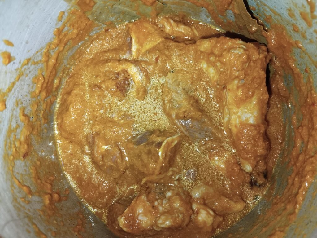 beef pieces covered in red spice paste cooking in pressure cooker for taro beef stew