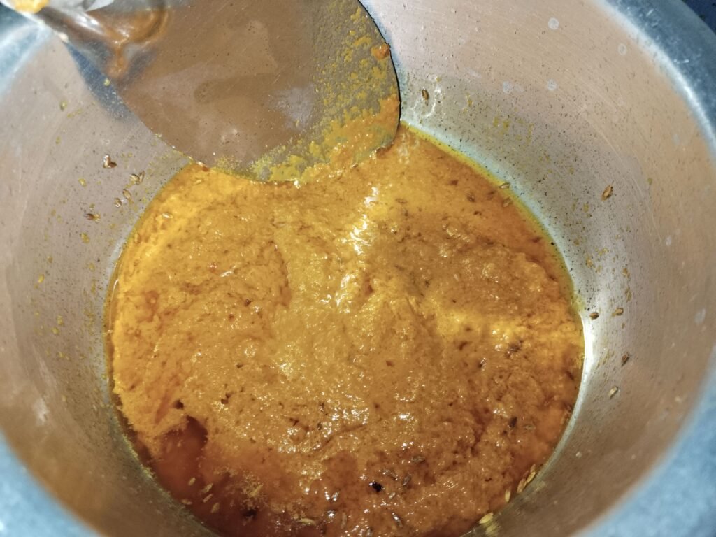 spice paste frying in oil in pot with spatula while cooking gravy