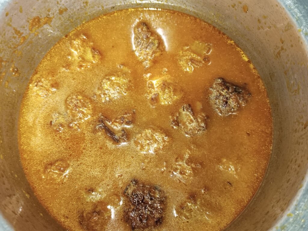 bottle gourd balls added to red orange spiced gravy in pot before garnish