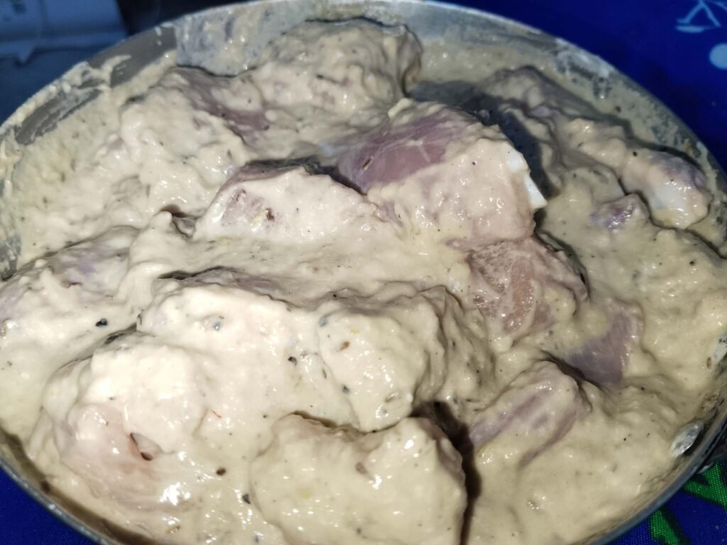 curd being spooned onto chicken pieces in bowl for white creamy chicken recipe marinade