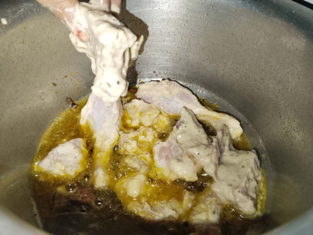 hand placing chicken piece into hot oil in pot while shaking off paste for white creamy chicken recipe
